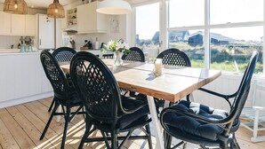 Cocina moderna con armarios blancos, una mesa de comedor de madera, sillas negras y ventanas amplias con vistas al campo.