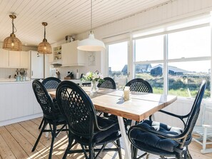 A modern kitchen with white cabinets, a wooden dining table, black chairs, and a large window offering a view of the countryside. - 4 Star Holiday Home in Skagen (Skagen)