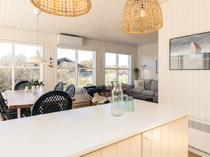 A room with a dining area, a sofa, and a large window with a view of the outdoors.