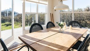 Comedor con una mesa de madera, sillas negras, una lámpara colgante y amplias ventanas que dan a zonas verdes y edificios.
