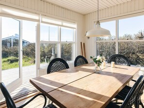 A dining area with a wooden table, black chairs, a vase with flowers, and large windows with a view of greenery and buildings. - 4 Star Holiday Home in Skagen (Skagen)
