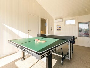 A ping pong table with a net, positioned in a room with white walls and a door leading to another room. - 4 Star Holiday Home in Skagen (Skagen)
