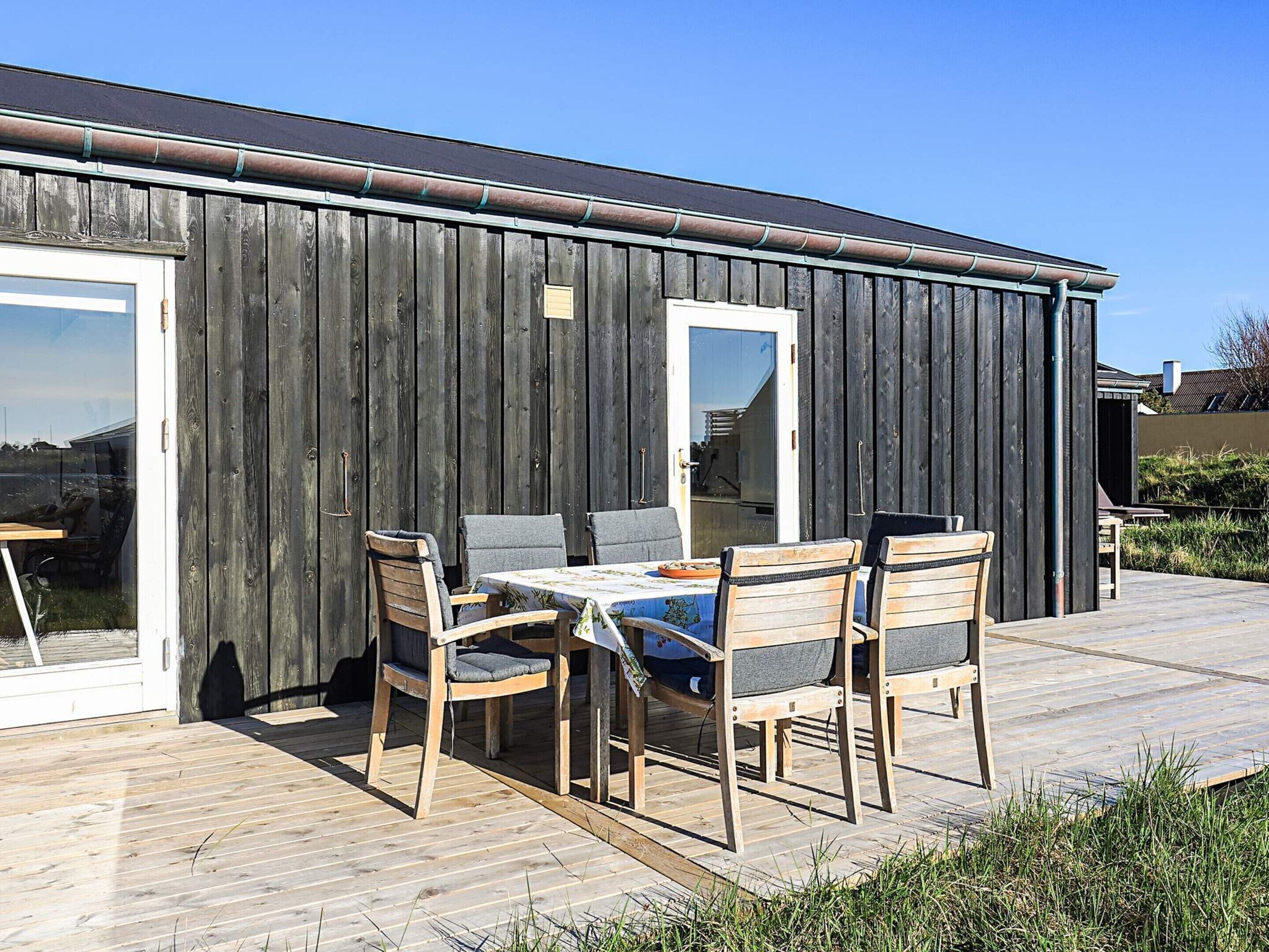 A wooden deck with a table and chairs, a door, and a window.