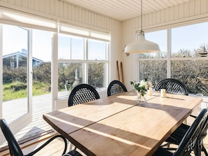 A dining area with a wooden table and chairs, large windows, and a hanging light fixture.