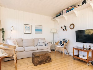 A cozy living room with a sofa, a coffee table, a wicker chair, a television, and a bookshelf with books and decorative items. - 4 Star Holiday Home in Skagen (Skagen)