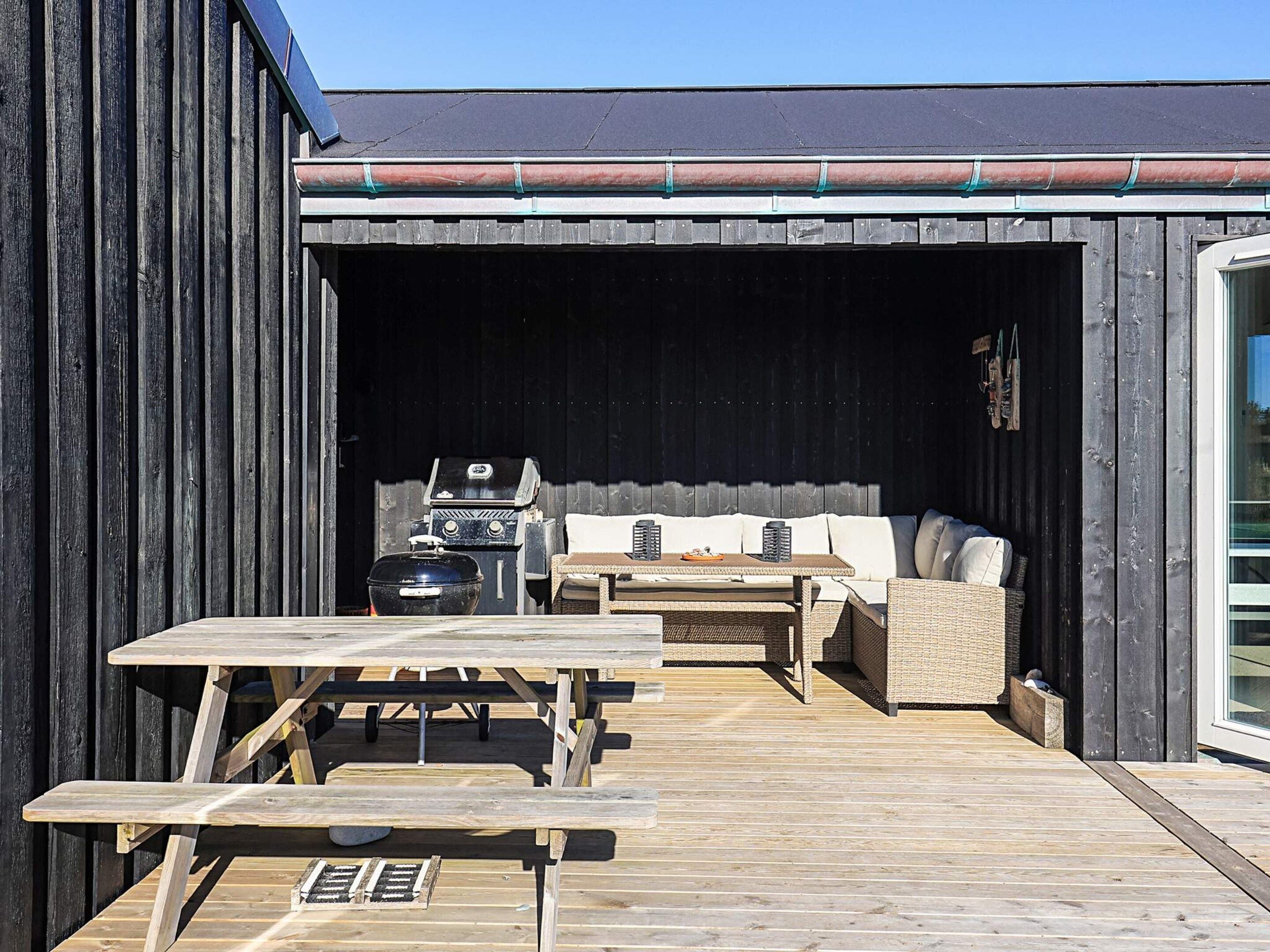Une terrasse extérieure avec une table et des bancs en bois, un barbecue et un canapé.