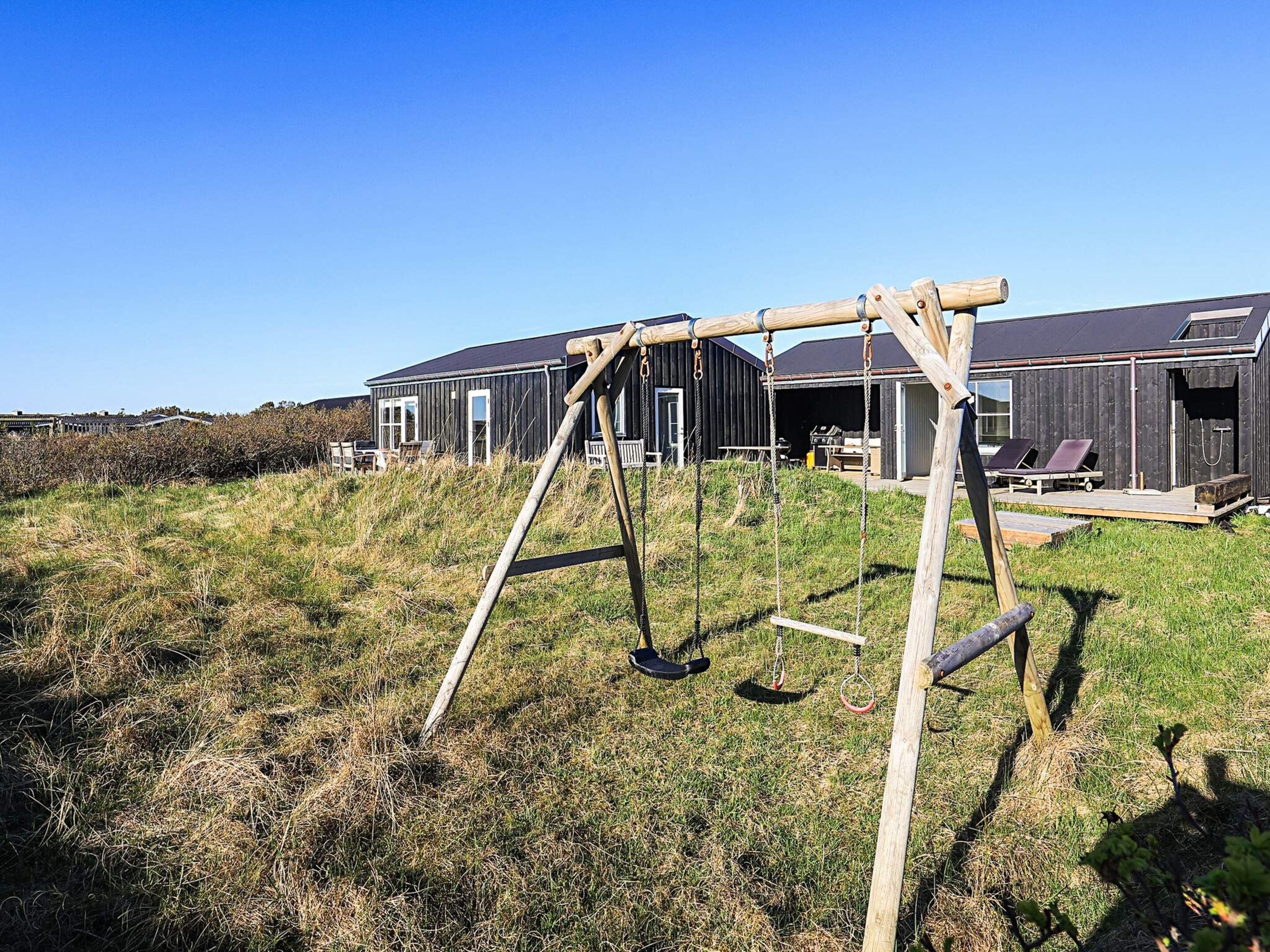 A wooden swing set in a grassy field with a modern building in the background.