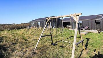A wooden swing set in a grassy field with a modern building in the background.