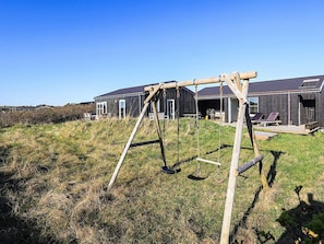A wooden swing set in a grassy field with a modern building in the background. - 4 Star Holiday Home in Skagen (Skagen)