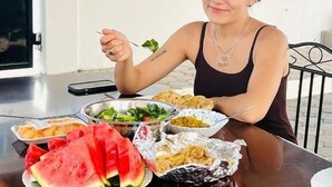 Una persona sentada en una mesa al aire libre con diversos platos, incluyendo sandía y una ensalada.