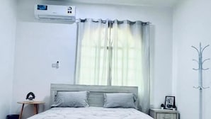 Un dormitorio con una cama grande, ventilador de techo, unidad de aire acondicionado, mesita de noche con lámpara y perchero.