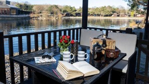 A table with a book, binoculars, a mug, a thermos, and a wicker basket on a balcony overlooking a lake. - Swanmere lodge, lakeside view cabin at Pinelake Carnforth (Carnforth)