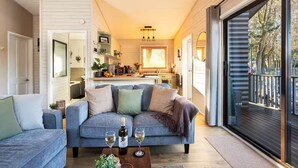 A cozy living room with a grey sofa, a coffee table with wine glasses, and a view of the kitchen and outside through a large sliding glass door. - Swanmere lodge, lakeside view cabin at Pinelake Carnforth (Carnforth)