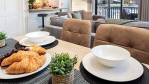 A cozy living room with a dining table set for breakfast, featuring croissants and a bowl. - Swanmere lodge, lakeside view cabin at Pinelake Carnforth (Carnforth)