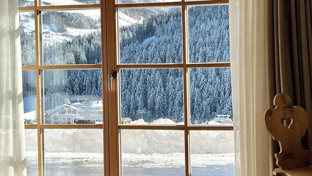 Een kamer met een grote schuifglazen deur en uitzicht op een besneeuwd berglandschap.