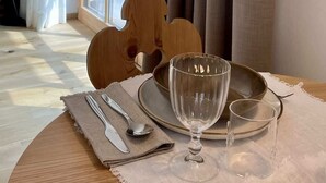 Een eethoek met een tafel gedekt voor twee personen, een raam met gordijnen, en uitzicht op groen.