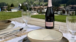 Een tafel voor twee gedekt met champagne, glazen en borden, met uitzicht op een bergachtig landschap.