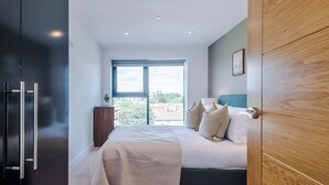 A modern bedroom with a large bed, a wooden wardrobe, and a window with a city view. - Premium City Penthouse Ideal For Business (Leeds)