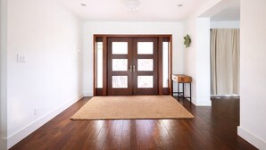 Una habitación amplia con piso de madera, una puerta grande con paneles de vidrio y una pequeña mesa de madera.