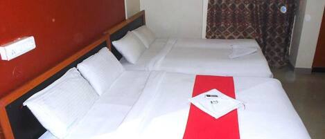 A hotel room with two beds, a red bed runner, white linens, a wooden headboard, and a patterned curtain.