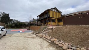 A two-story building with a balcony, a parking area, and a red and blue sports court. - Buho Cabin Studio BBQ Kitchen Parking Pool (La Serena)