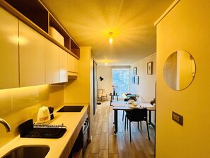 A compact kitchen with a dining area, a view through the window, and a round mirror on the wall. - Buho Urban Curic A C Washer Dryer Wifi (Santiago)