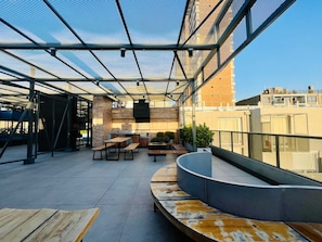 Una terraza en la azotea de diseño moderno, con un área de estar que incluye bancos y mesas, una parrilla y plantas en macetas.