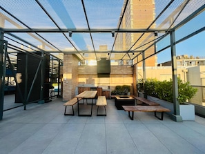An outdoor patio with a glass ceiling, wooden tables and benches, and a brick wall. - Buho Urban Curic A C Washer Dryer Wifi (Santiago)