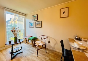 A small dining area with a table, chairs, and a window with a view of buildings. - Buho Urban Curic A C Washer Dryer Wifi (Santiago)