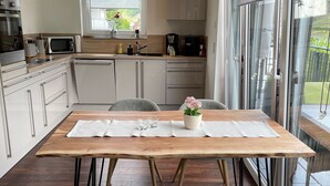 A modern kitchen with a dining area, featuring a wooden table, grey chairs, and a view through large windows. - 5 star (DTV) vacation apartment ''Auszeit''- directly on the Moselle with large balcony (Oberfell)