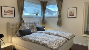 A bedroom with a large bed, two side tables, a nightstand, a window with curtains, and framed pictures on the walls. - 5 star (DTV) vacation apartment ''Auszeit''- directly on the Moselle with large balcony (Oberfell)