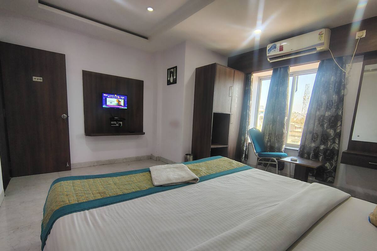 A hotel room with a bed, a TV mounted on the wall, a wardrobe, and an air conditioning unit.