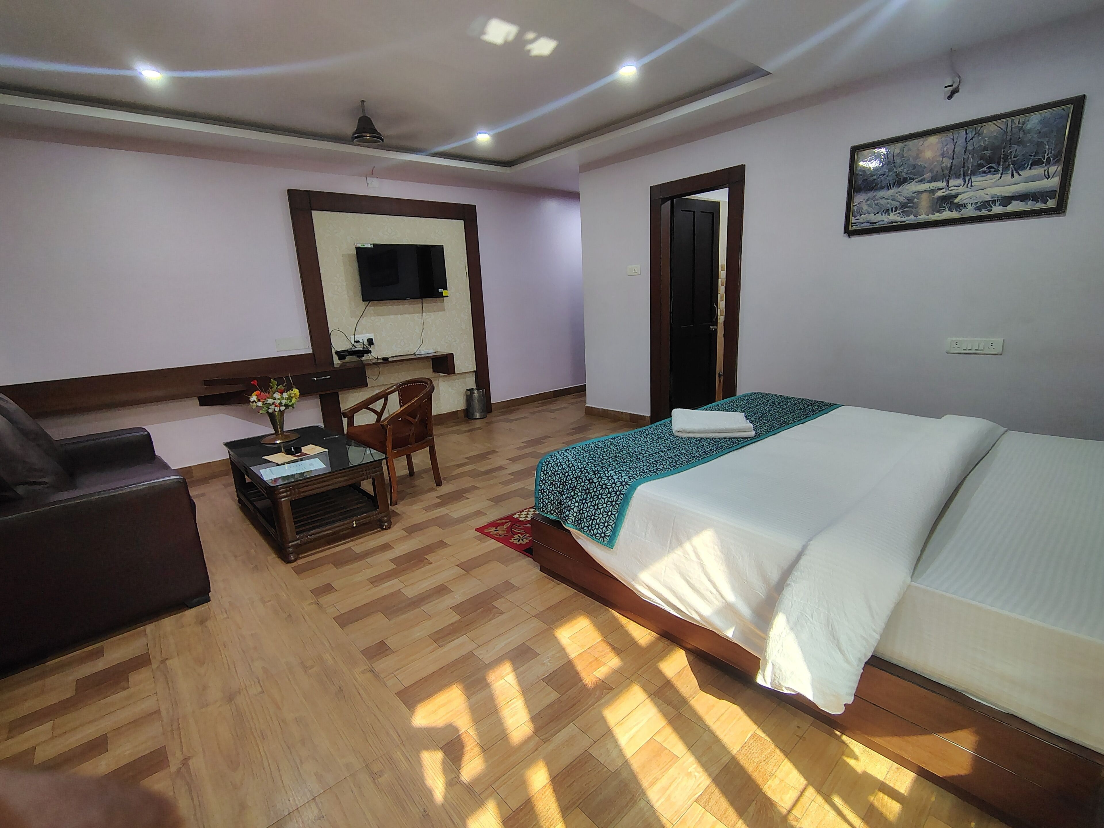A hotel room with a bed, a desk, a chair, a TV mounted on the wall, and a painting.