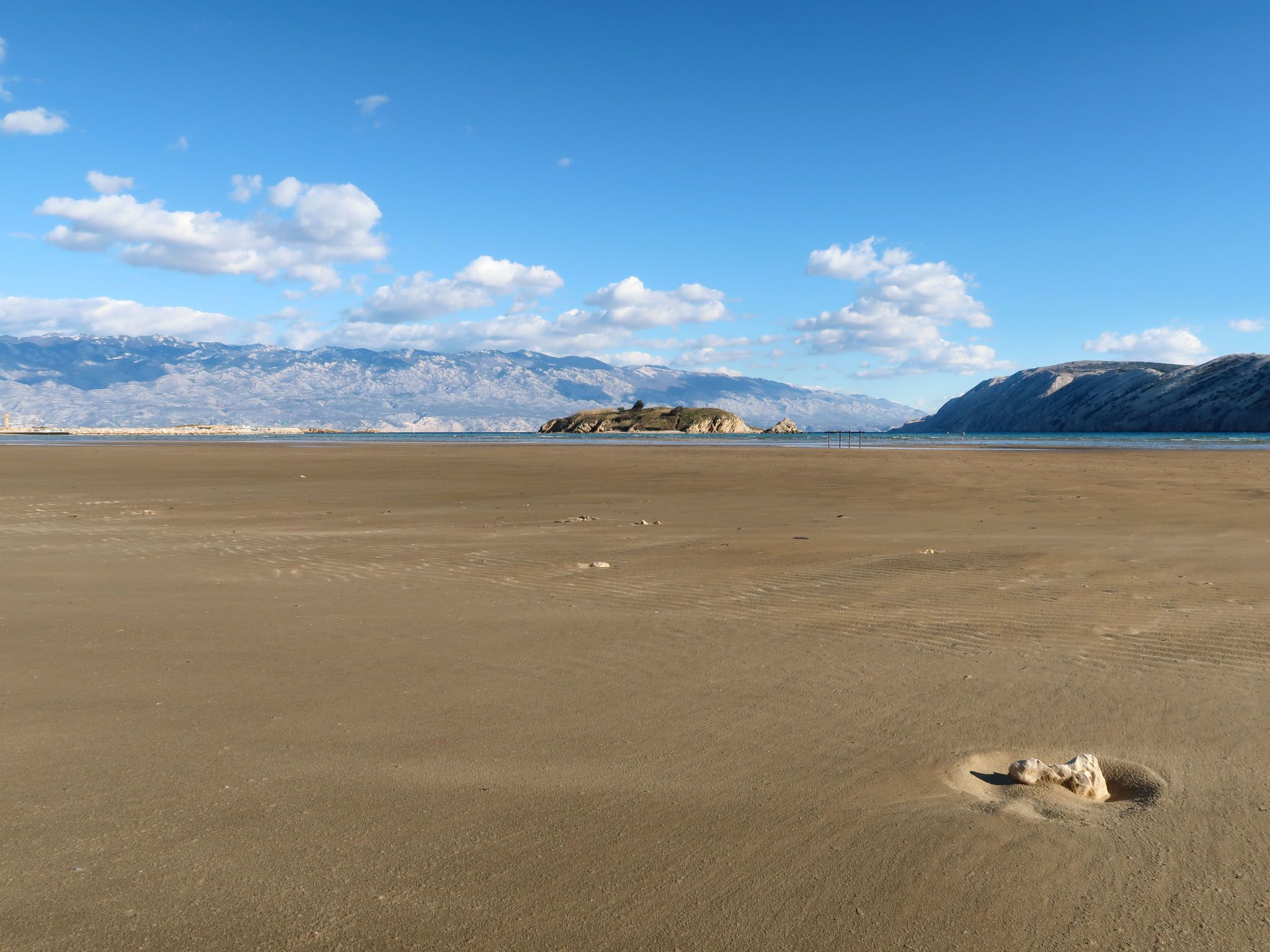 A wide, open sandy beach with a clear sky and distant mountains.