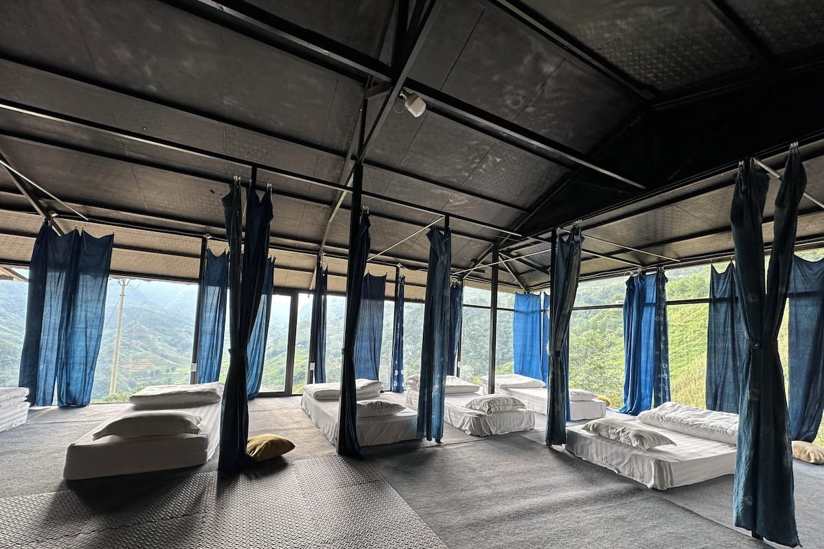 Une chambre avec quatre lits, chacun doté d’un baldaquin, et une grande fenêtre offrant une vue sur les montagnes.