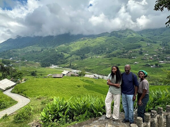 A group of people standing on a stone platform overlooking a lush green valley with terraced fields and a few buildings in the distance. - Nomadtrails Lodge (Sa Pa)