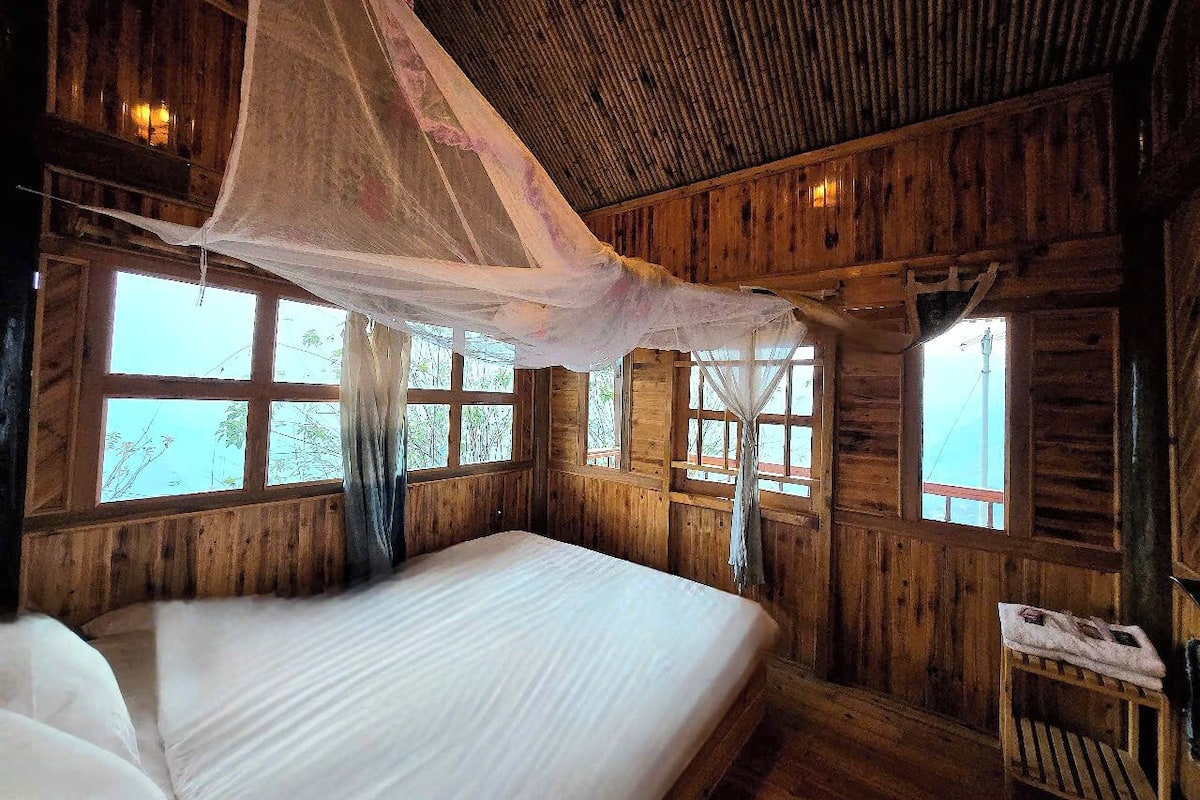 Une chambre dans une cabane en bois, avec un grand lit, des fenêtres et une moustiquaire.