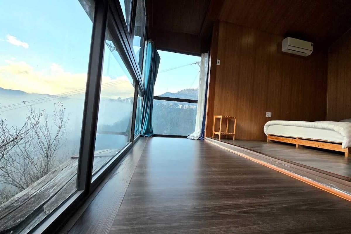 Une chambre avec une grande fenêtre, un lit et un plancher en bois.