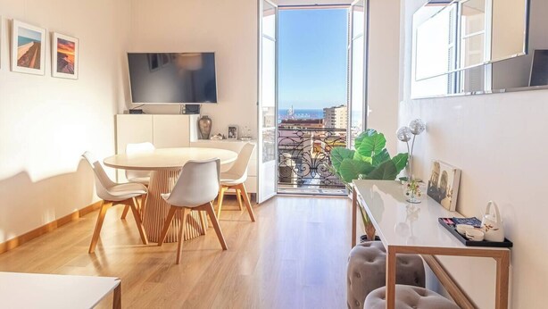 Una sala de estar moderna con comedor, televisor de pantalla plana y balcón con vista a la ciudad.