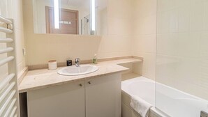 Un baño con lavamanos blanco, un espejo, toallero y bañera.