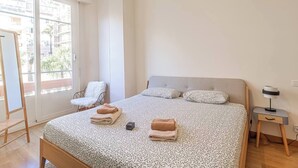 Un dormitorio con una cama grande, una silla, un escritorio y una ventana con vista a edificios.