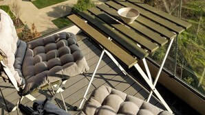 A balcony with a cushioned chair and a table, overlooking a residential area with modern buildings and a small garden. - Parcului20 Apart near Romexpo, Herastrau Park (București)