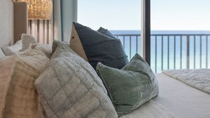 En säng med kuddar, en hängande lampa och utsikt över havet.