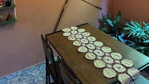 A dining area with a wooden table, crocheted placemats, and various potted plants.