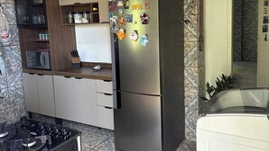 A kitchen with a stainless steel refrigerator, a stove, and cabinets. There are decorative magnets on the refrigerator, and a potted plant on the counter.
