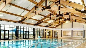 Ein Innenpool mit großen Glaswänden, Holzbalken und Fliesenboden.