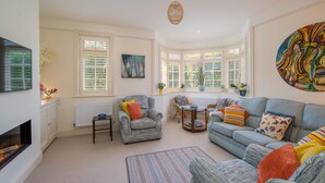 A cozy living room with a fireplace, comfortable seating, and large windows. - Nine Buoys - sleeps 10 guests near the beach (Bembridge)