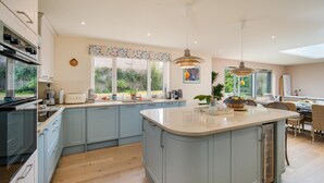 A modern kitchen with light blue cabinets, a central island, and a dining area with wicker furniture. - Nine Buoys - sleeps 10 guests near the beach (Bembridge)