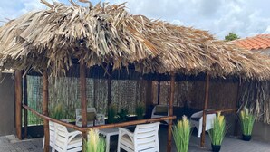 Un espace extérieur aménagé avec des sièges, protégé par un auvent, comprenant des chaises blanches et des plantes en pot.