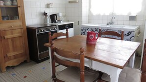 Una cucina con un tavolo di legno, sedie, una tazza rossa, un fornello e un armadietto.